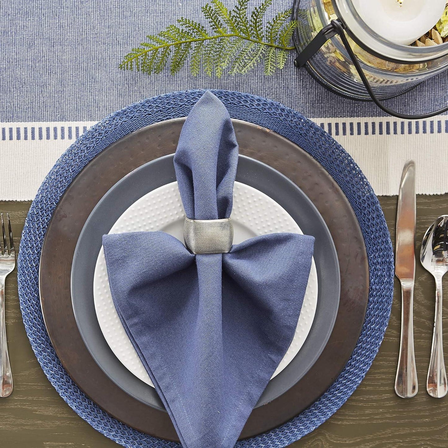 Elegant table setting with blue napkin, plates, and cutlery on a patterned tablecloth.