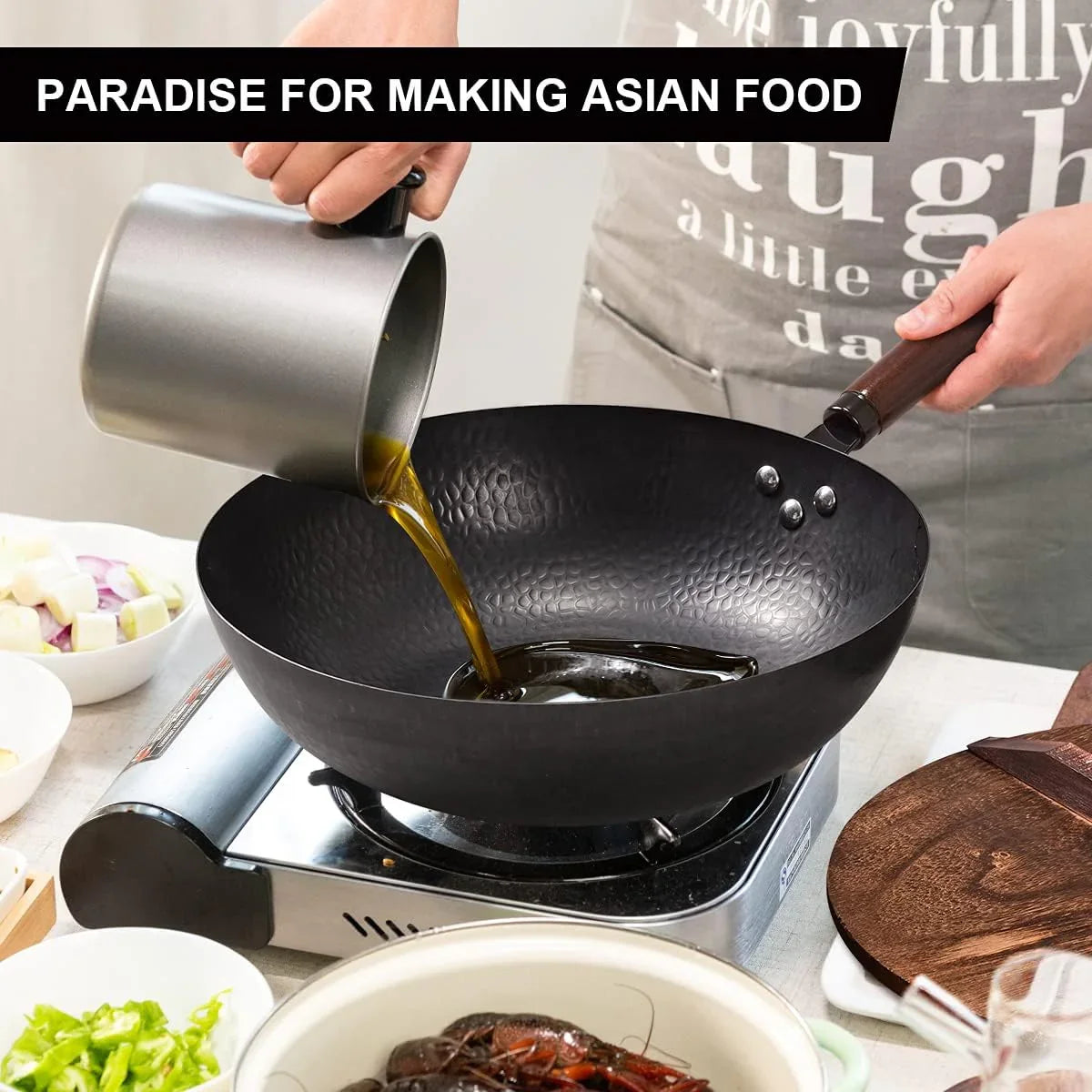 Person pouring oil into 12.8-inch black carbon steel flat-bottom wok on portable gas stove with cooking ingredients nearby