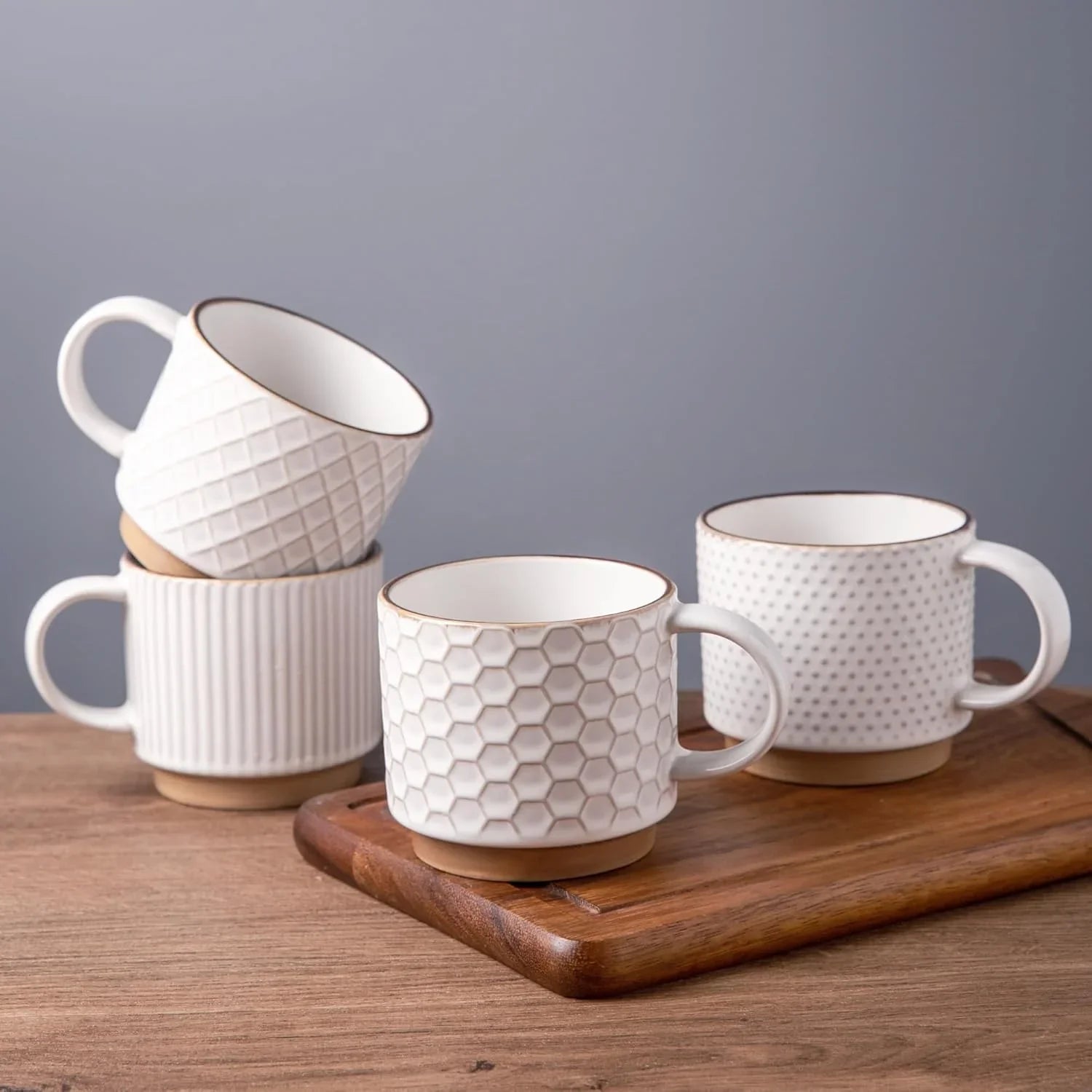 Set of four 12oz white textured ceramic coffee mugs with wooden bases on wooden tray and table