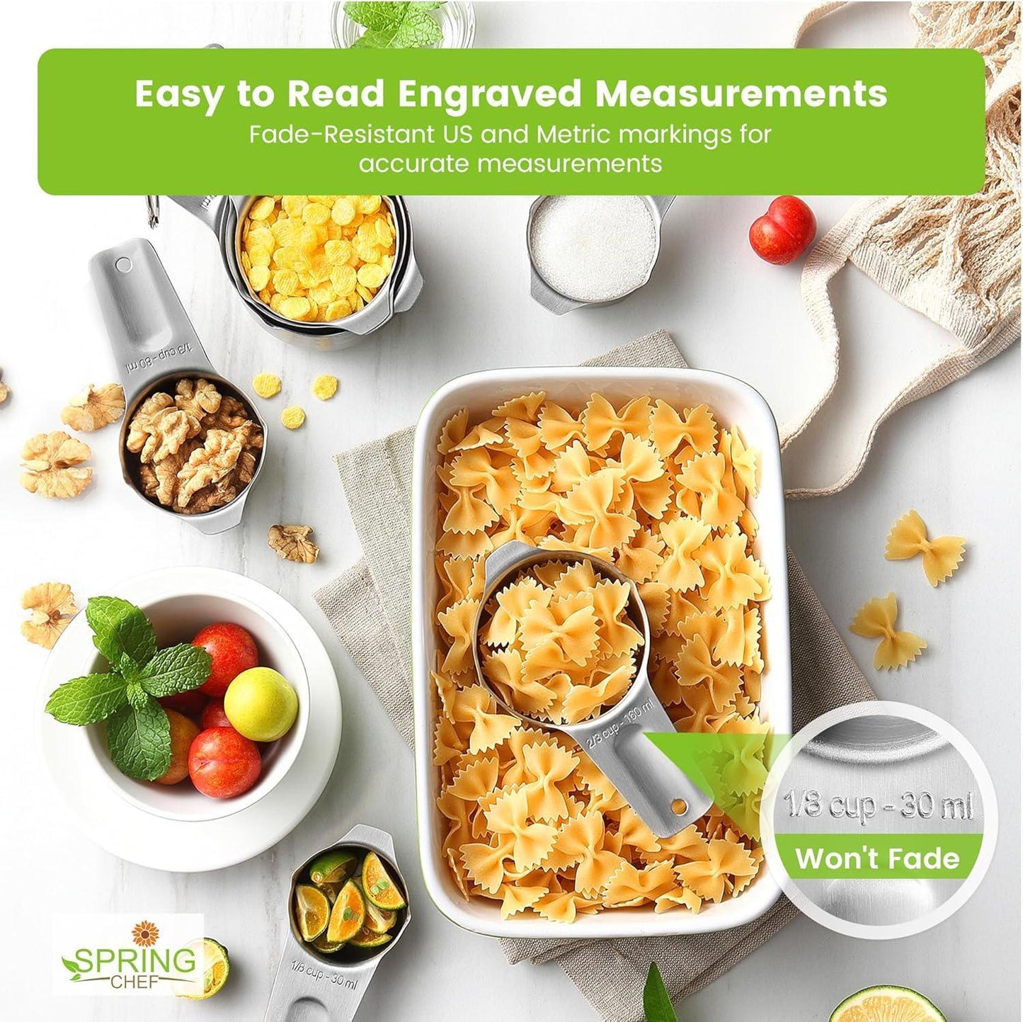 Stainless steel measuring cups with engraved measurements filled with pasta, nuts, fruit, and cereal on a white surface