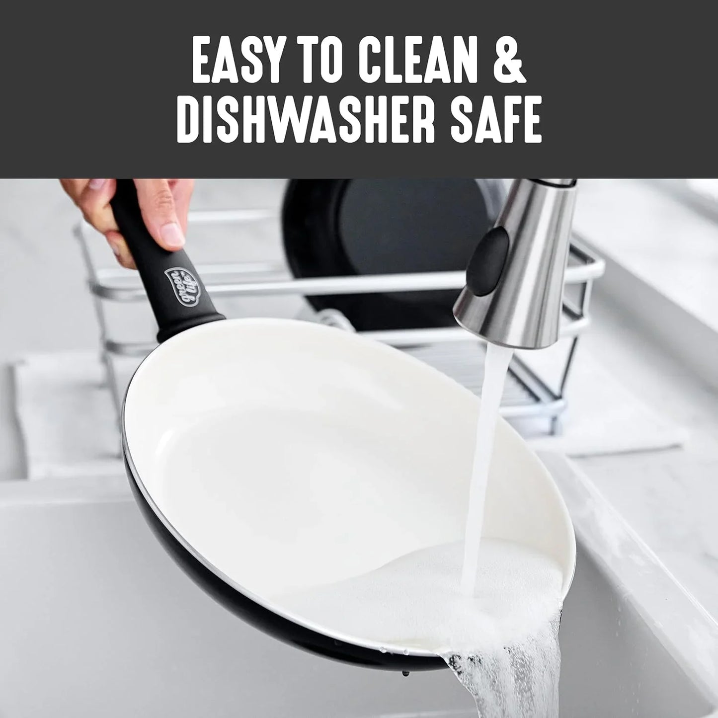 Hand holding black handle ceramic nonstick frying pan being rinsed with water in kitchen sink