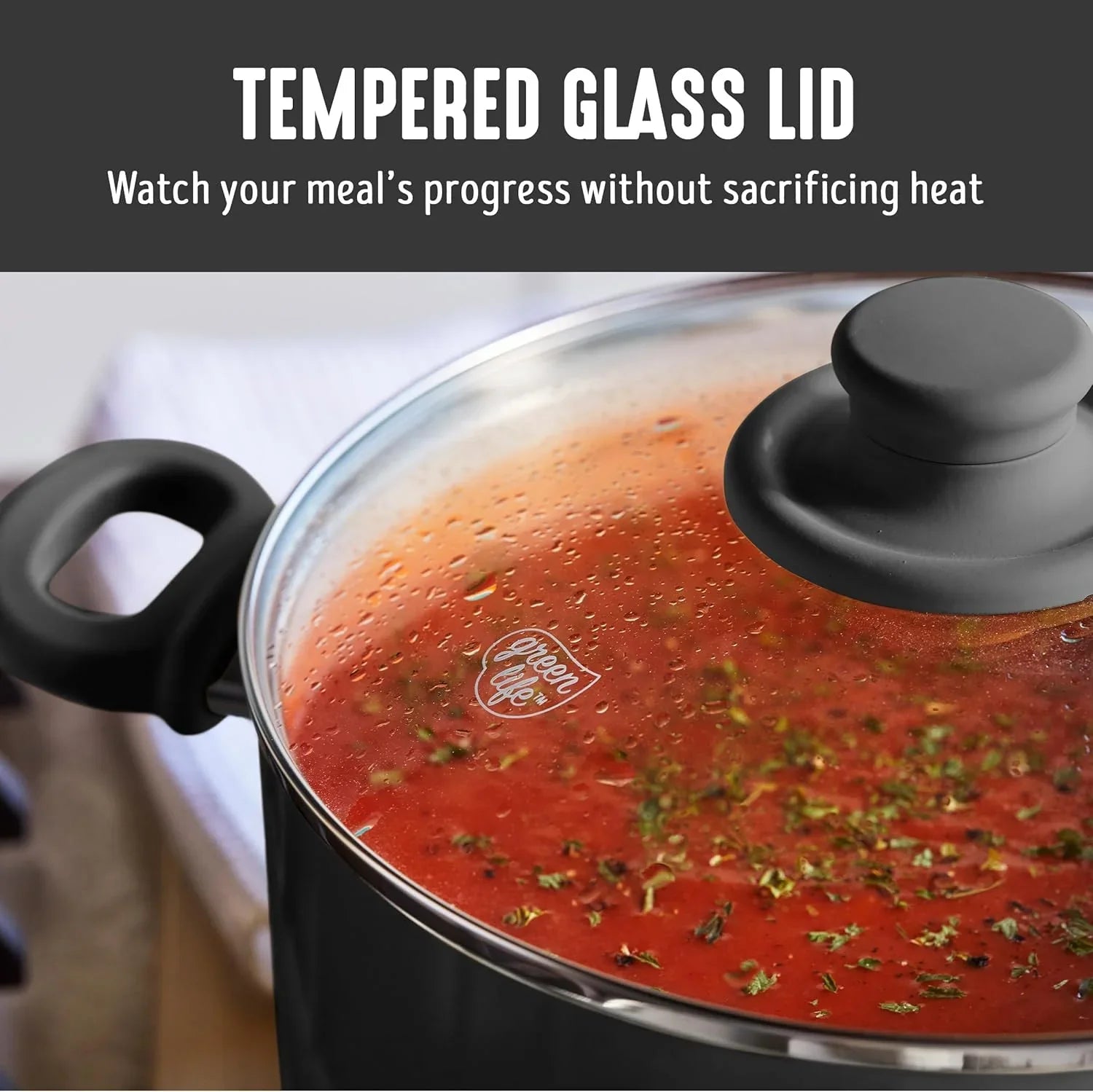 Close-up of black pot with tempered glass lid showing tomato soup with herbs inside