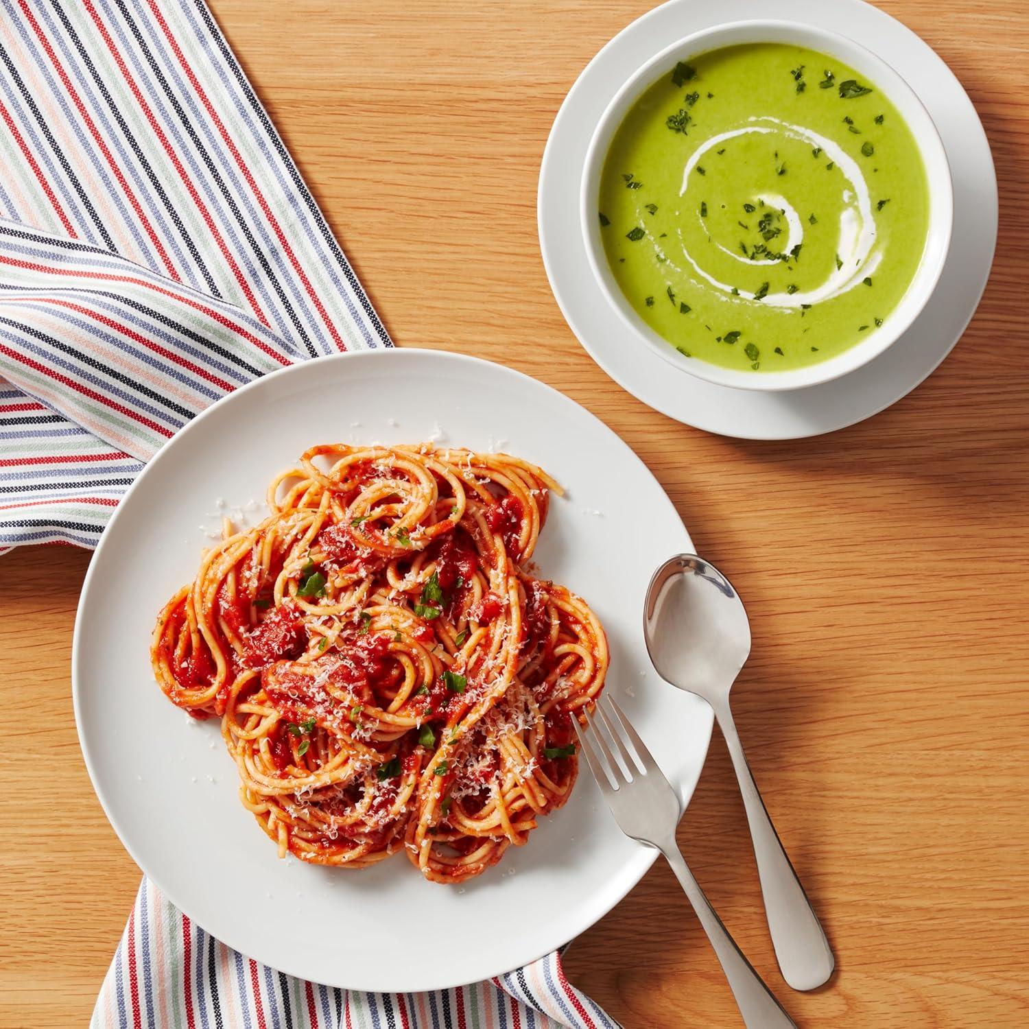 White porcelain plate with spaghetti marinara and grated cheese, bowl of green soup with cream swirl, fork and spoon on wooden table