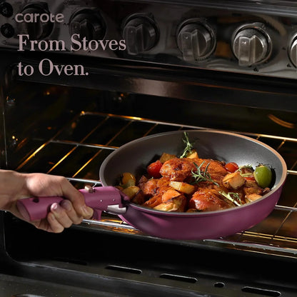 Hand placing a purple nonstick pan with roasted chicken and vegetables into an oven, stove knobs visible