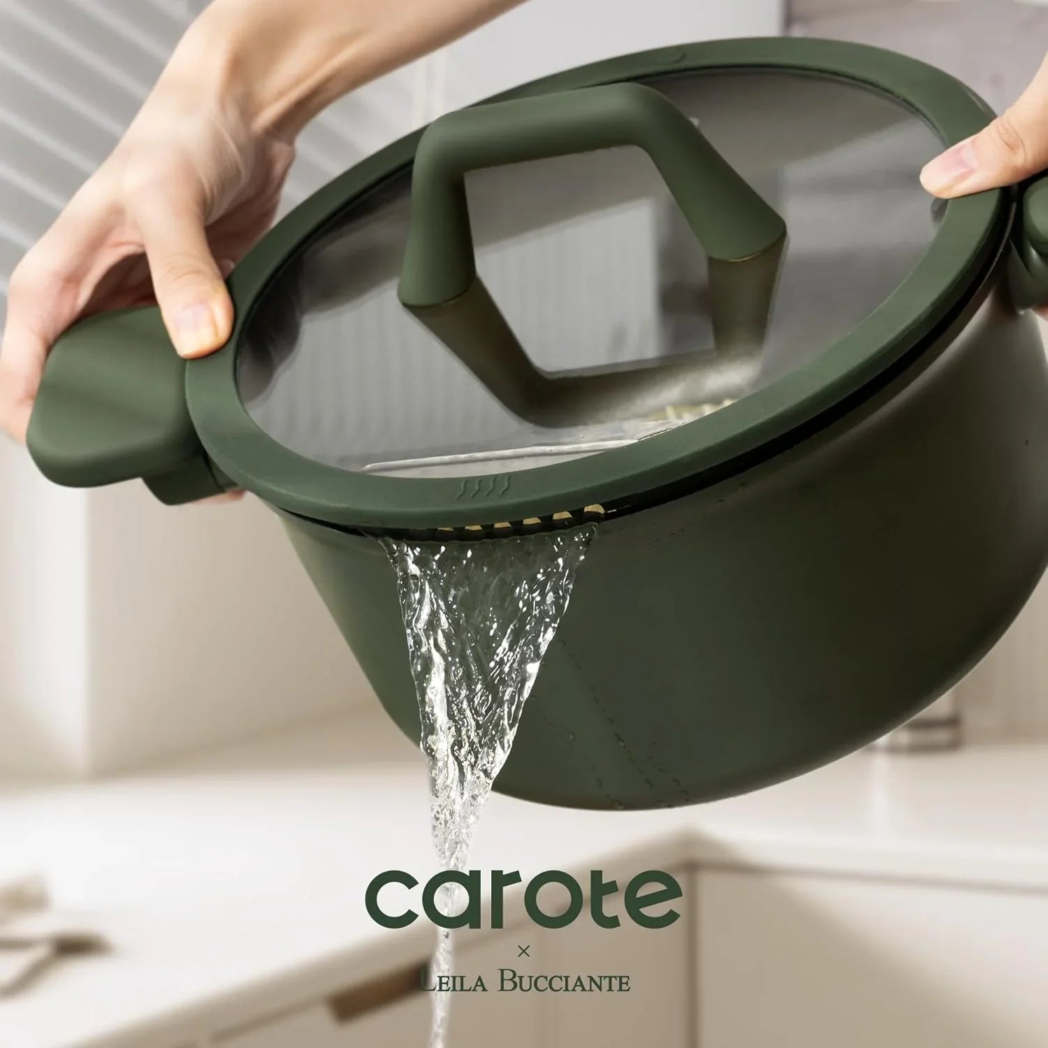 Green pot with glass lid draining water through built-in strainer in modern kitchen