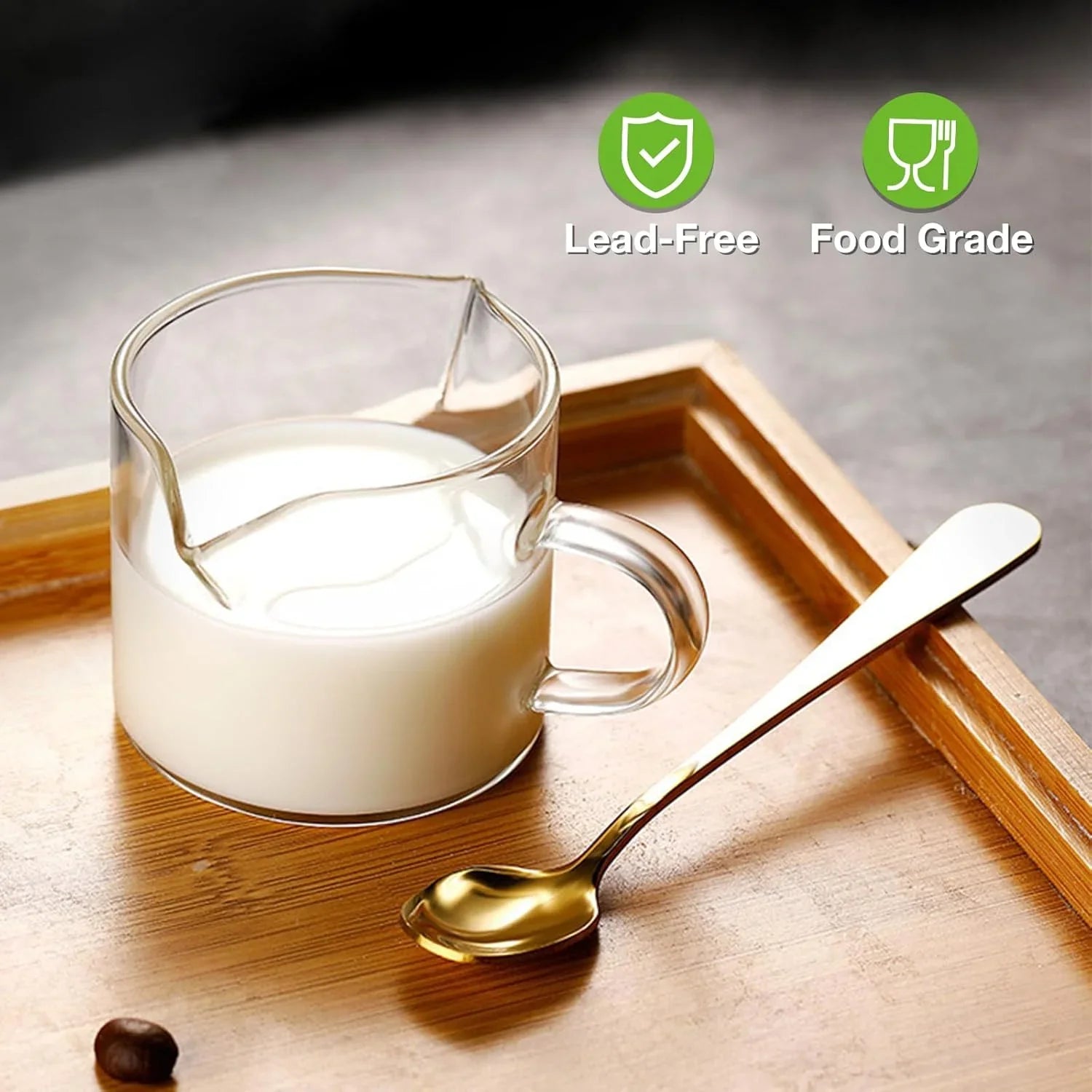 Clear double spout glass cup filled with milk on a wooden tray with a gold spoon