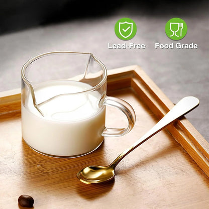 Clear double spout glass cup filled with milk on a wooden tray with a gold spoon