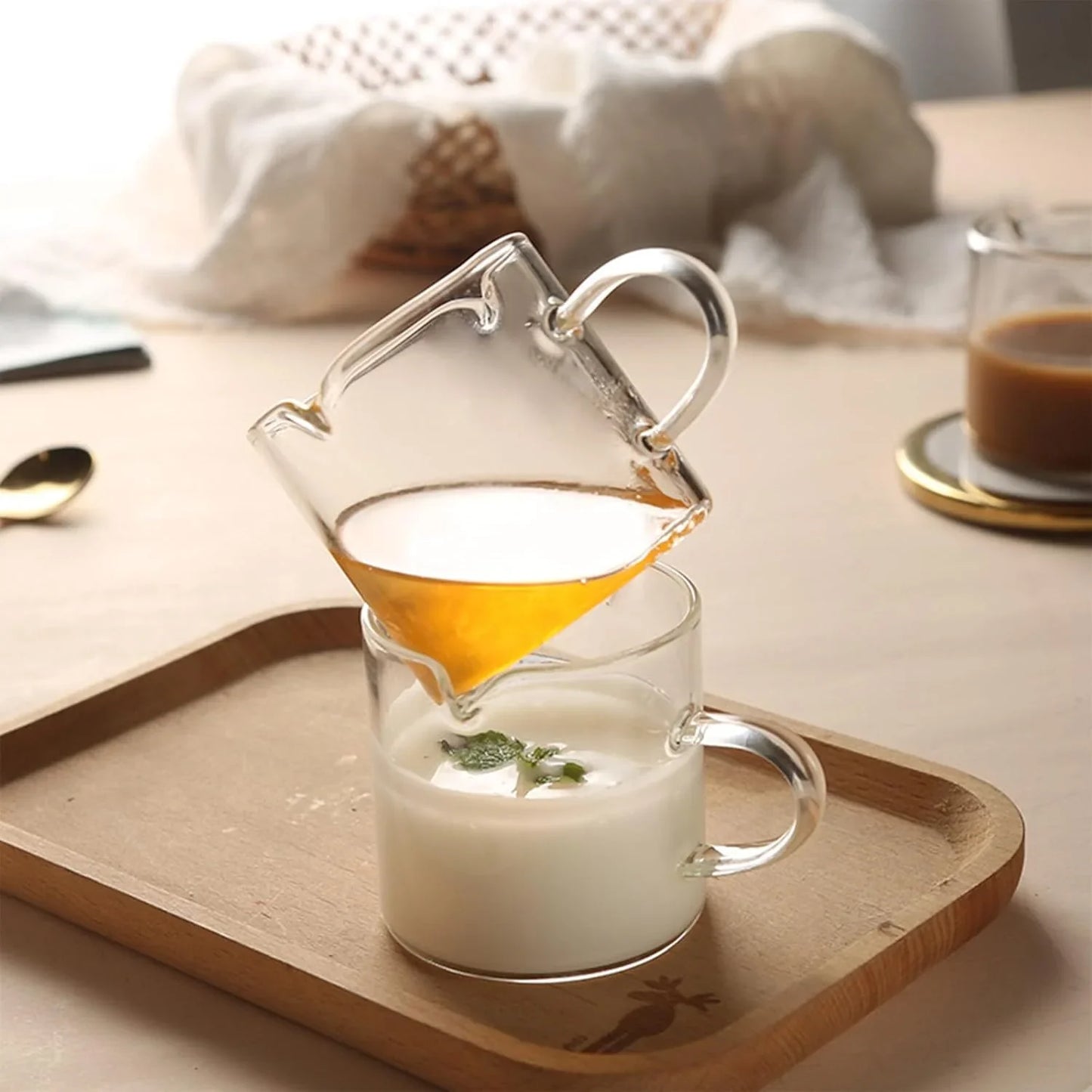 Clear borosilicate glass double-spout espresso cup pouring honey into glass cup with yogurt on wooden tray