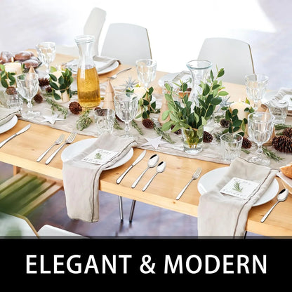 Elegant modern dining table set with silver stainless steel flatware, glassware, candles, and greenery centerpiece