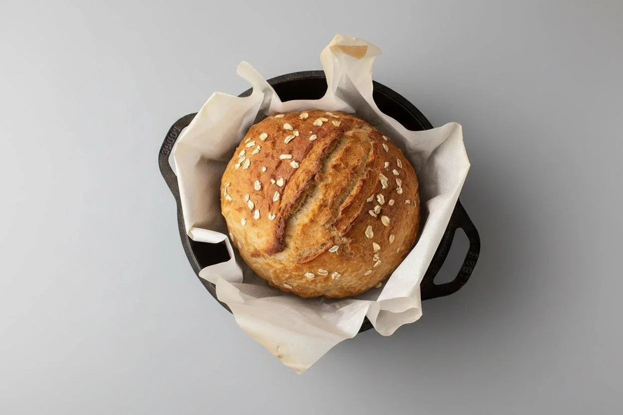 Freshly baked oat-topped round bread in a black cast iron Dutch oven lined with parchment paper