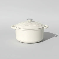 Cream white enameled cast iron Dutch oven with lid and stainless steel knob on light background