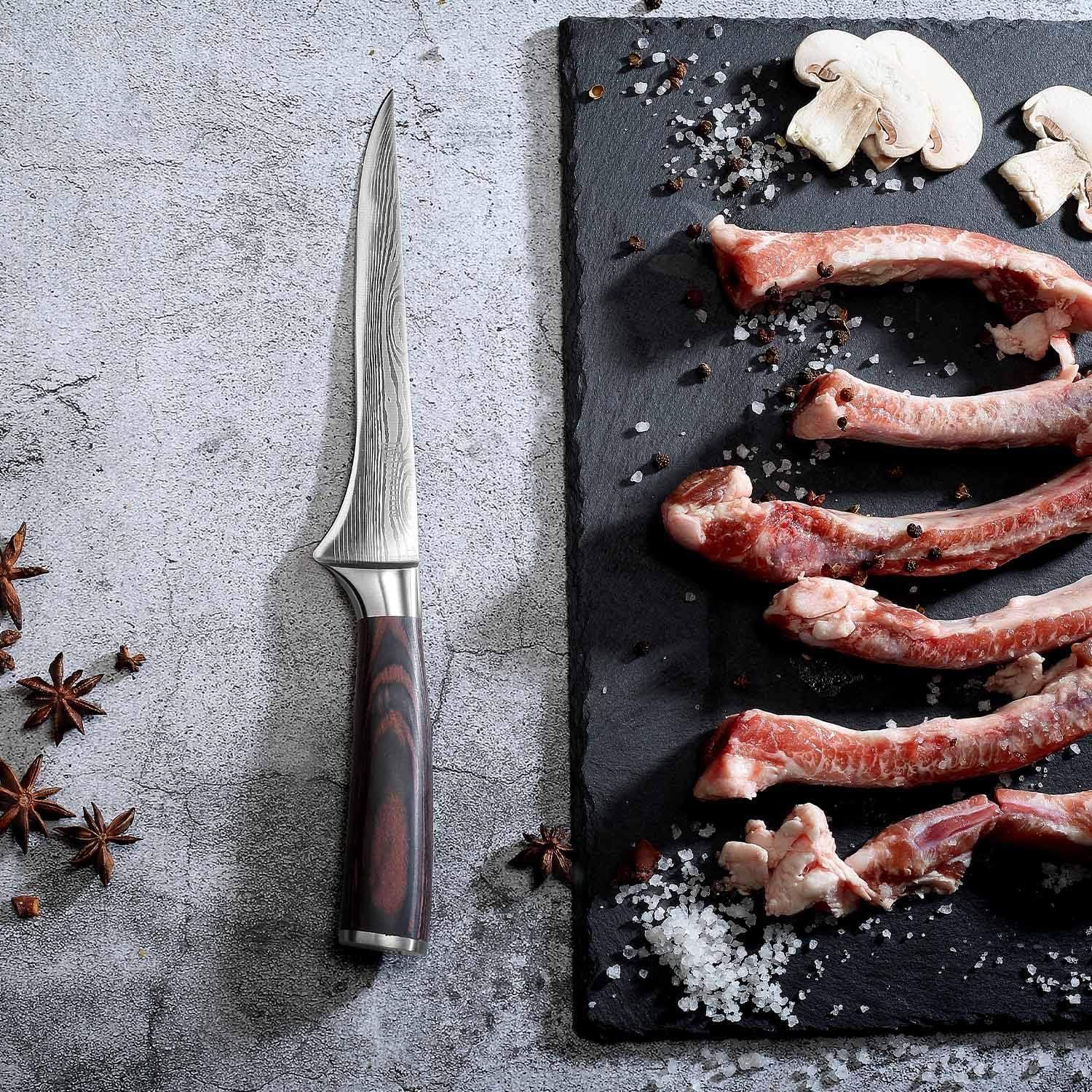 6-inch super sharp German boning knife with wooden handle next to raw meat ribs, mushrooms, and spices on slate