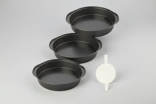 Set of three black 6-inch nonstick round cake pans with handles and parchment paper circles on white background