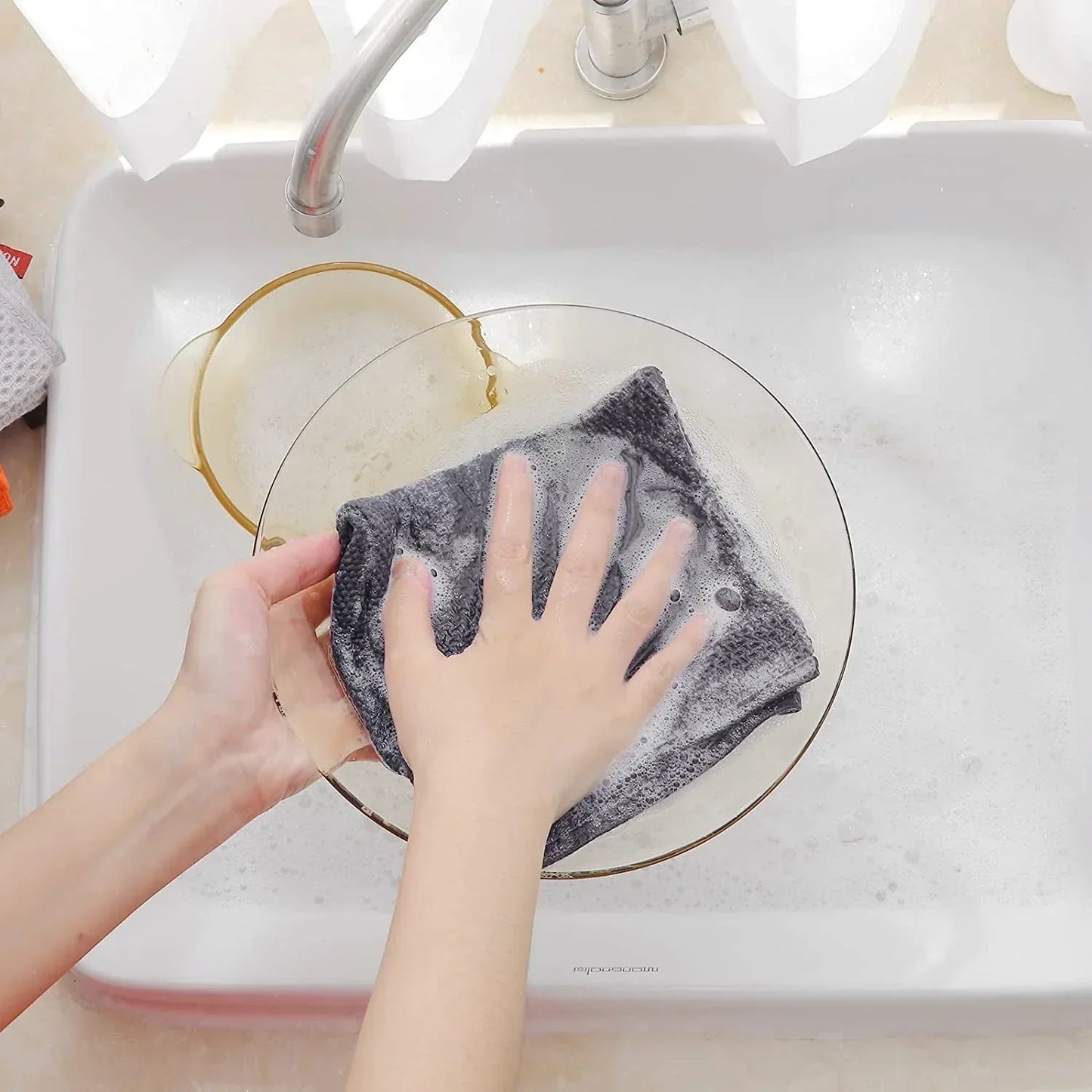 Person washing glass bowl with dark grey cotton waffle weave dish cloth in white kitchen sink