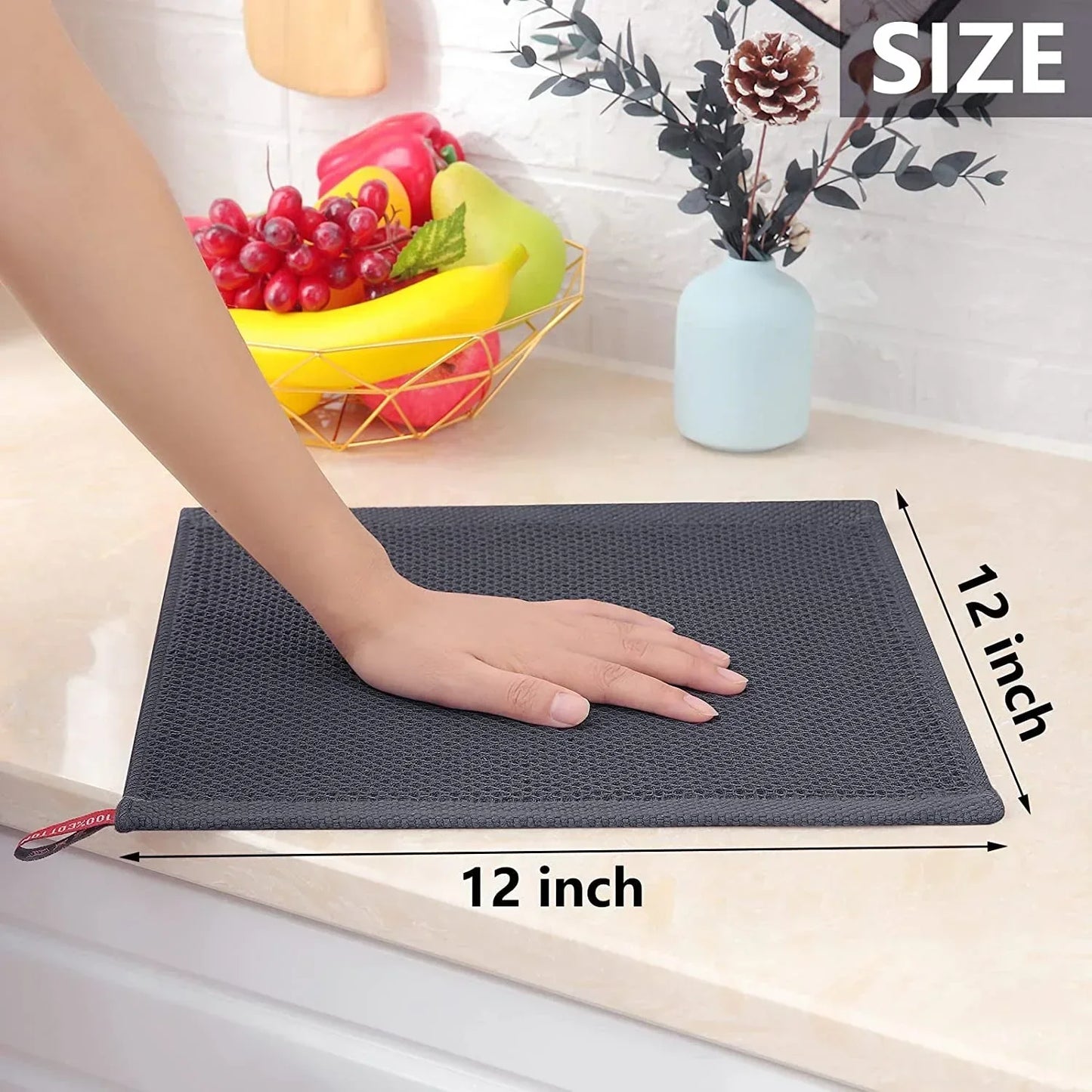 Hand measuring 12x12 inch dark grey waffle weave kitchen dish cloth on countertop with fruit basket and vase