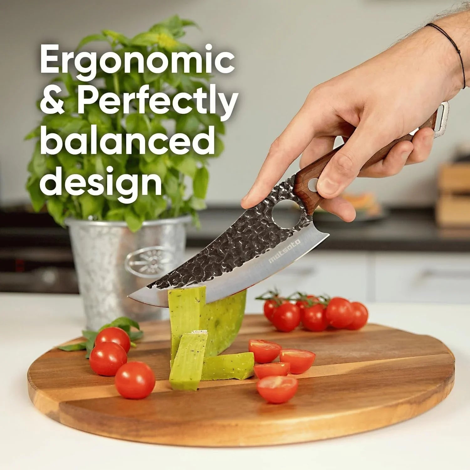 Hand holding a hammer-textured chef knife slicing cactus on wooden cutting board with cherry tomatoes