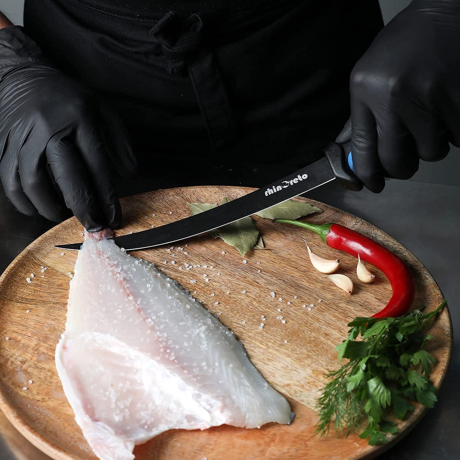 Hand in black gloves slicing fish fillet on wooden board with flexible fillet knife, chili, garlic, and herbs
