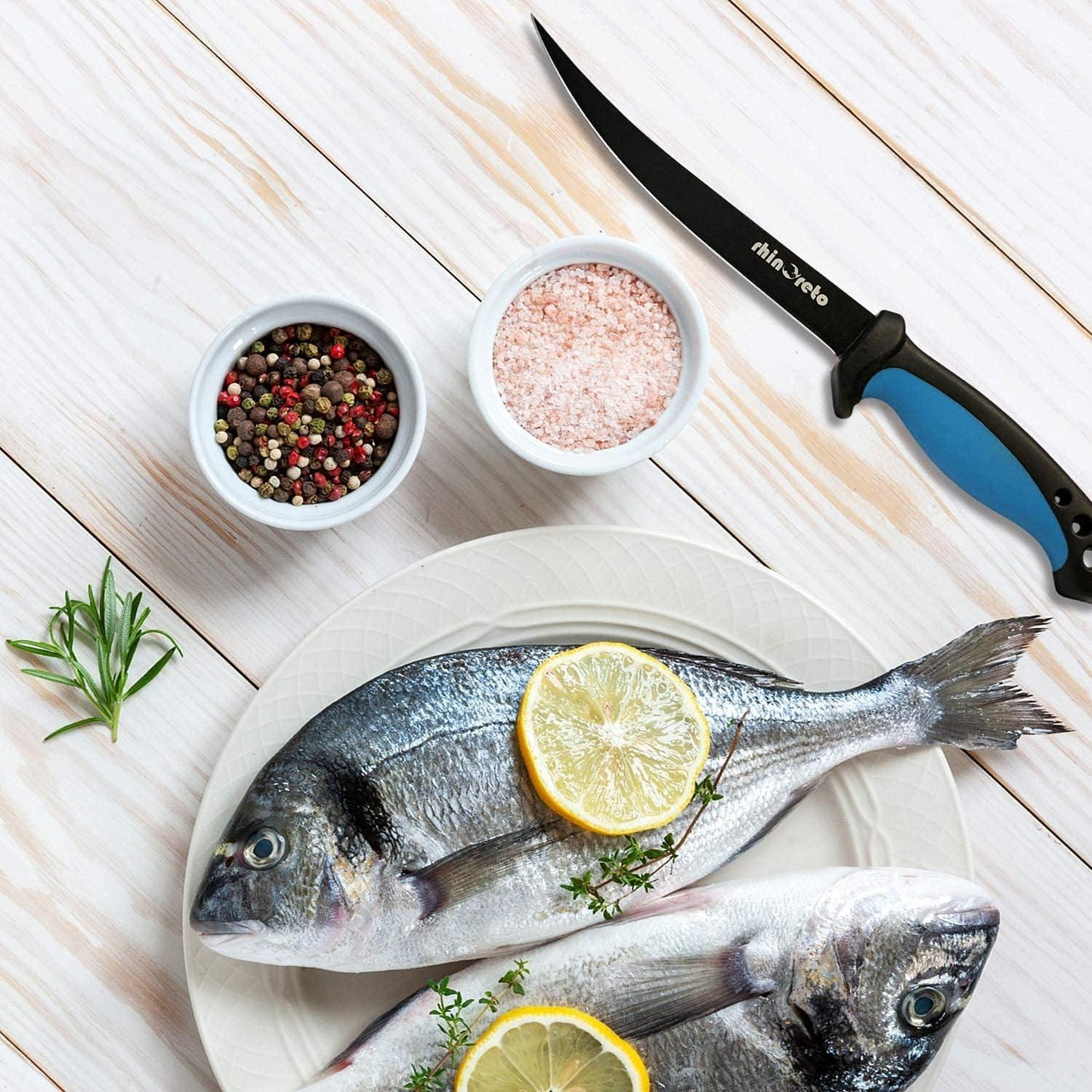 Fresh whole fish on a plate with lemon slices, herbs, pink salt, peppercorns, and a flexible fillet knife