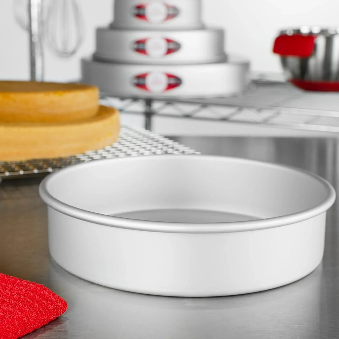 8-inch anodized aluminum round cake pan on stainless steel countertop with baked cake layers and baking tools