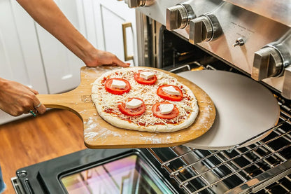 Person sliding raw pizza with tomato, cheese on bamboo peel into oven with stone baking surface