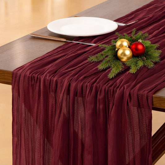 Burgundy table runner with Christmas decorations on a wooden table.