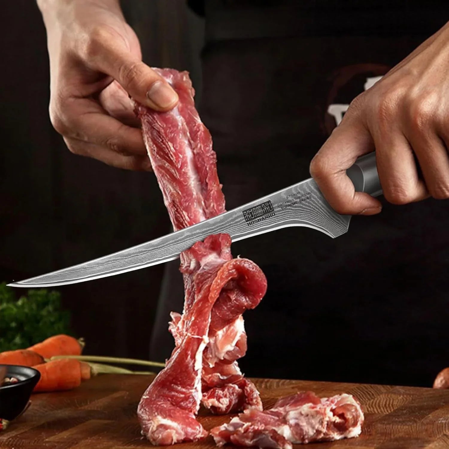 Hand using Damascus fillet knife to slice raw meat on wooden cutting board with carrots in background
