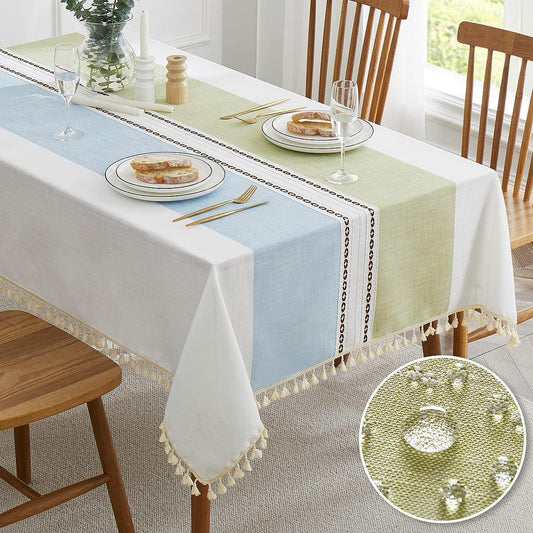 Dining table with a light blue and green tablecloth, wooden chairs, and a close-up of water droplets on the fabric.