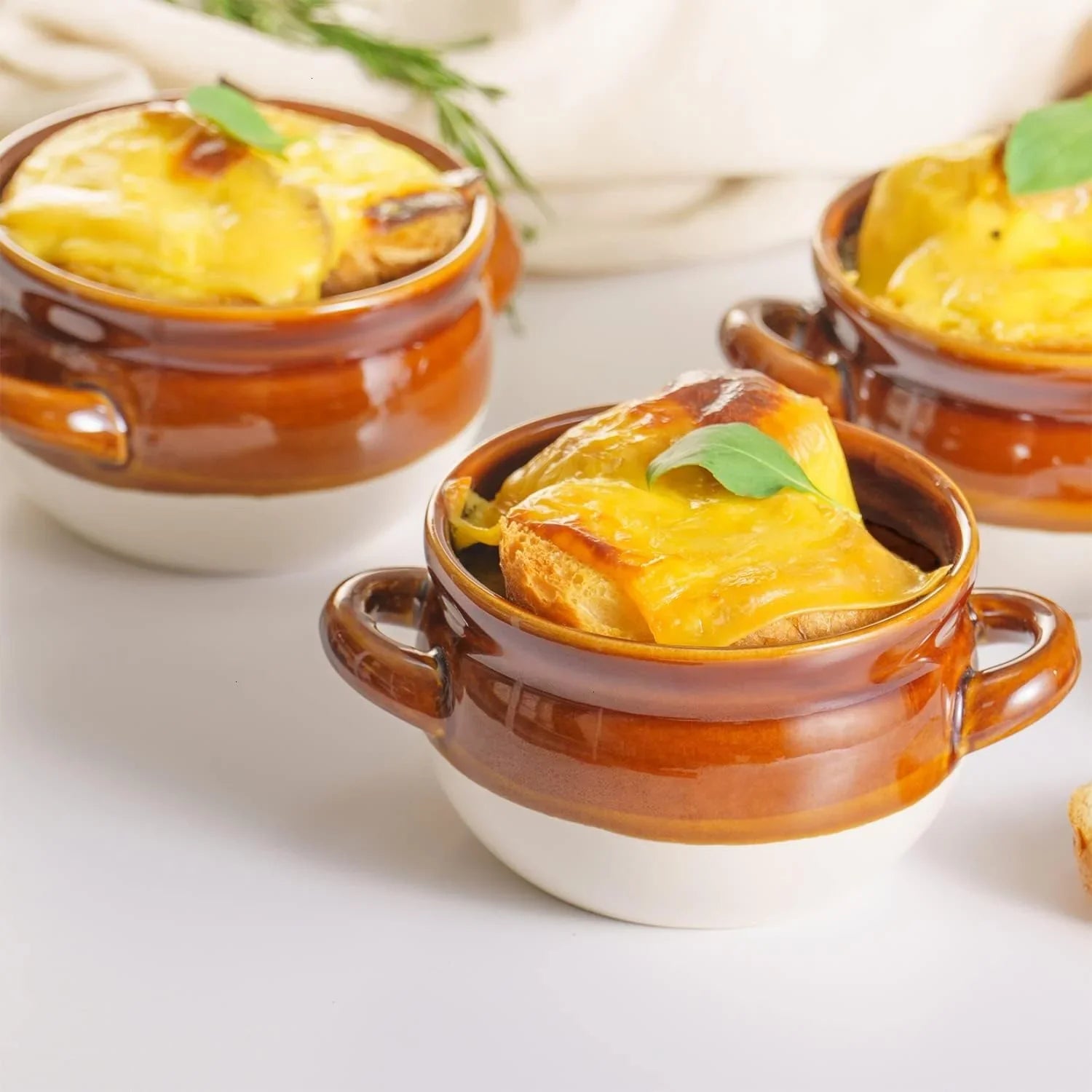French onion soup served in brown and white ceramic crocks with melted cheese and a basil leaf garnish