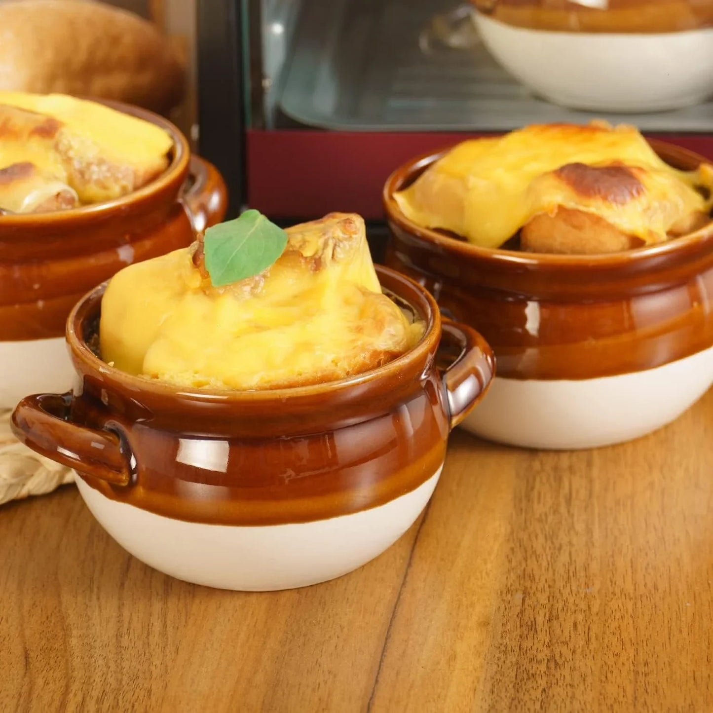 Set of four ceramic brown and white French onion soup bowls with handles on wooden table