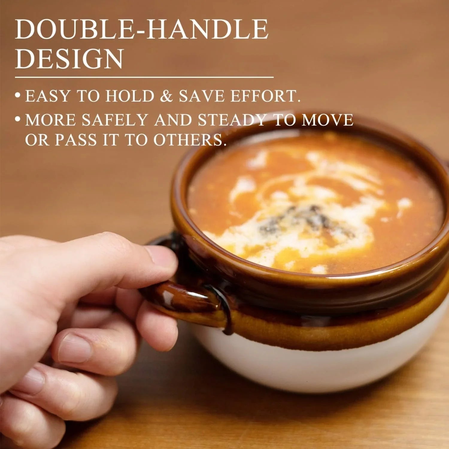 Hand holding brown and white ceramic double-handle soup bowl filled with creamy soup on wooden table