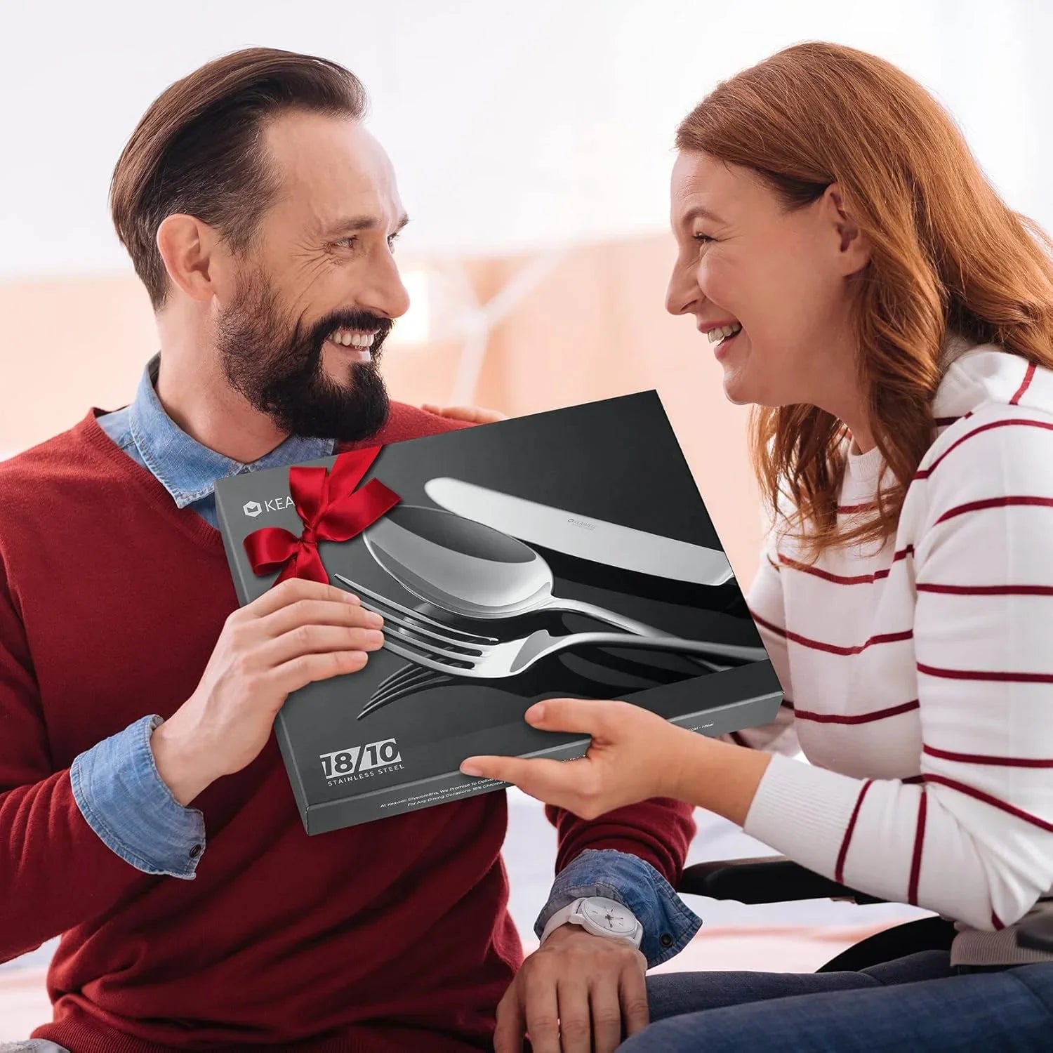 Man in red sweater happily receiving 18/10 stainless steel flatware gift set from smiling woman