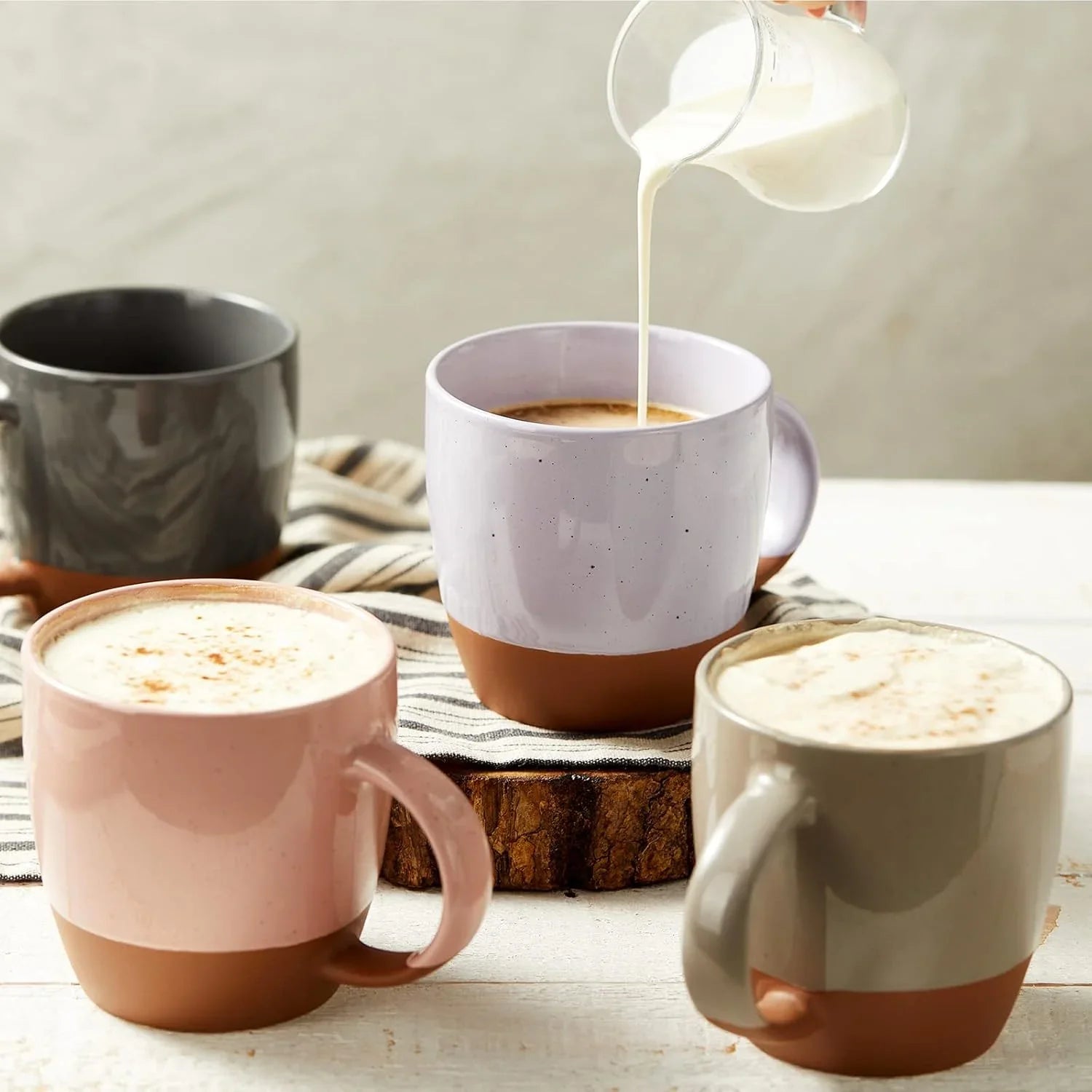 Set of four large Morandi color ceramic coffee mugs with brown base, one being poured cream