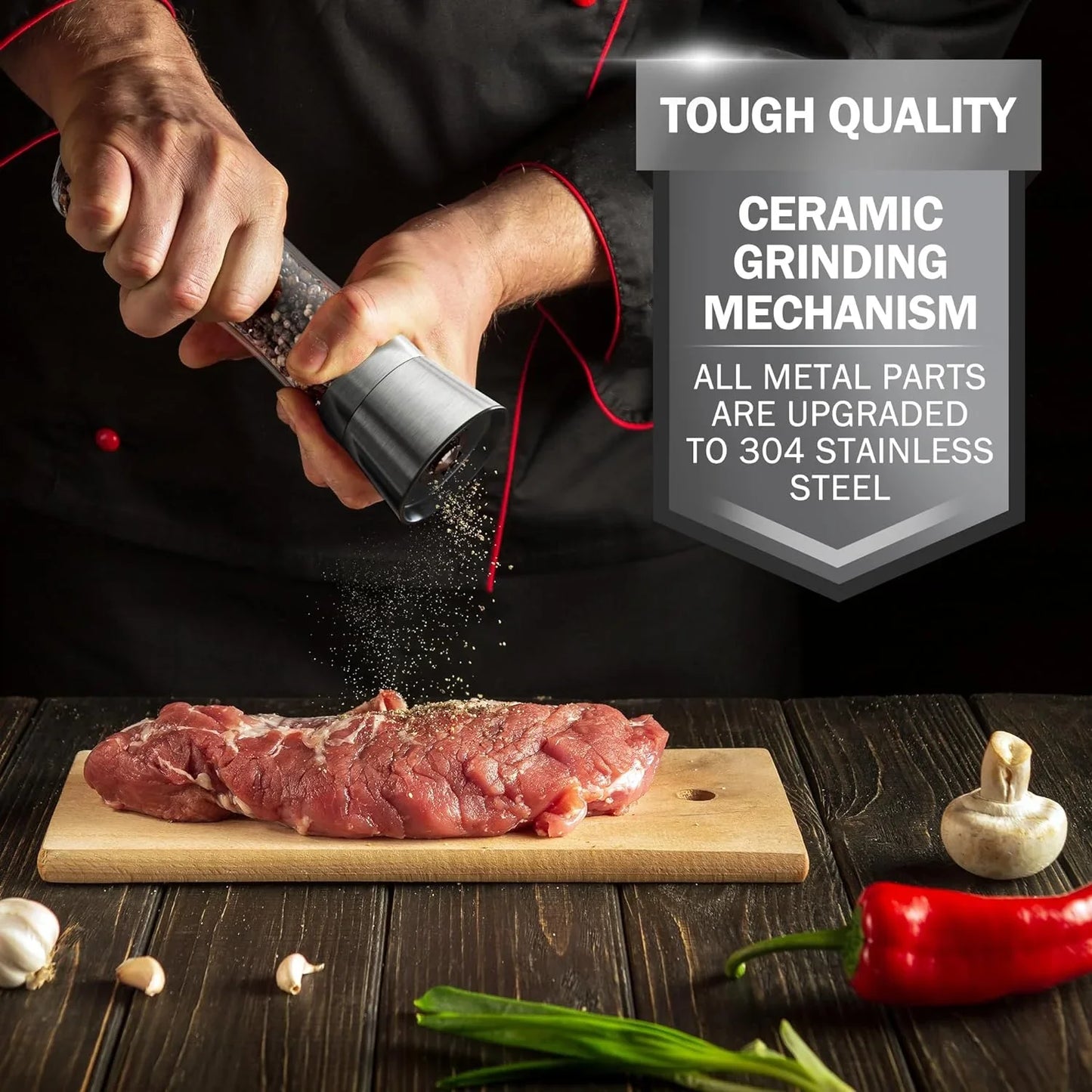 Hand using stainless steel pepper grinder to season raw meat on wooden cutting board with garlic, chili, and mushroom