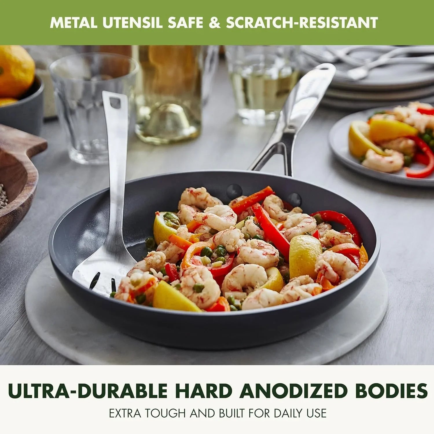 Hard anodized nonstick fry pan with cooked shrimp, bell peppers, lemon wedges, metal spatula on marble surface