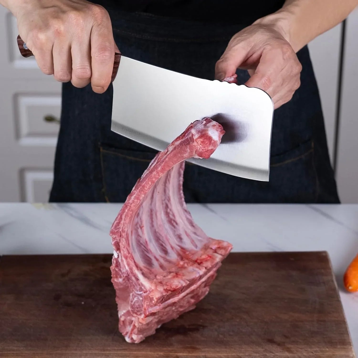 Person holding a 7-inch heavy-duty meat cleaver over a rack of raw ribs on a wooden cutting board