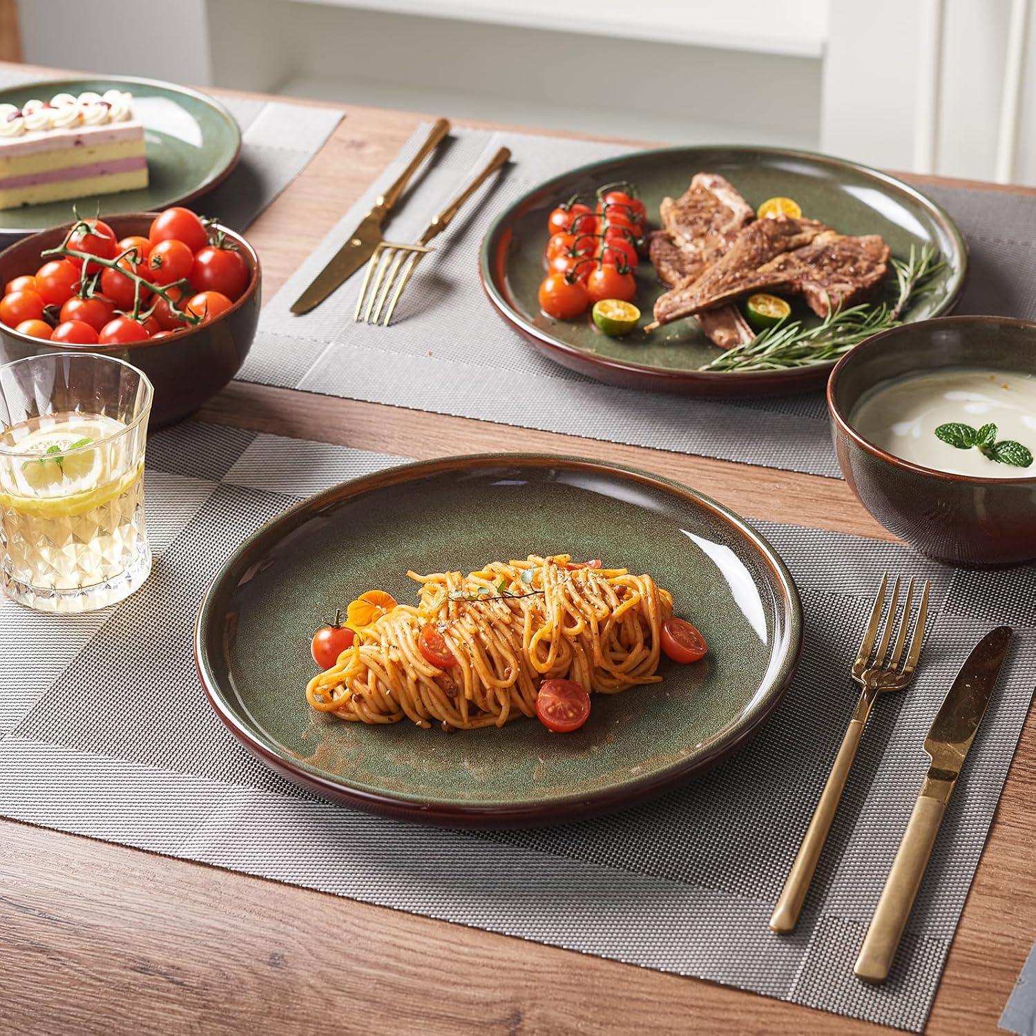 Brown and green reactive glaze stoneware dinnerware set with pasta, grilled meat, cherry tomatoes, soup, and lemon drink on wooden table
