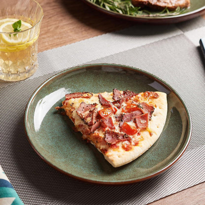 Slice of ham and tomato pizza on green reactive glaze stoneware plate on wooden table