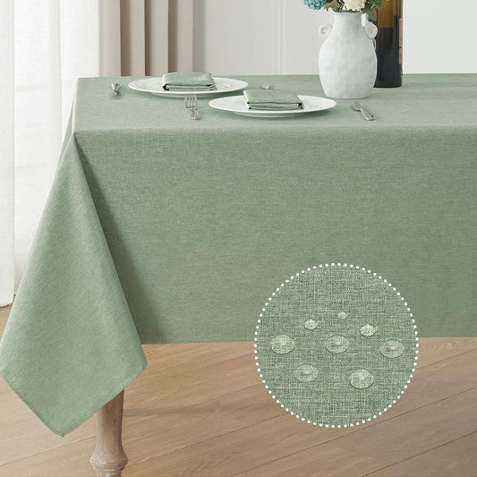 Sage green waterproof linen textured rectangular tablecloth on wooden table with two place settings and floral vase