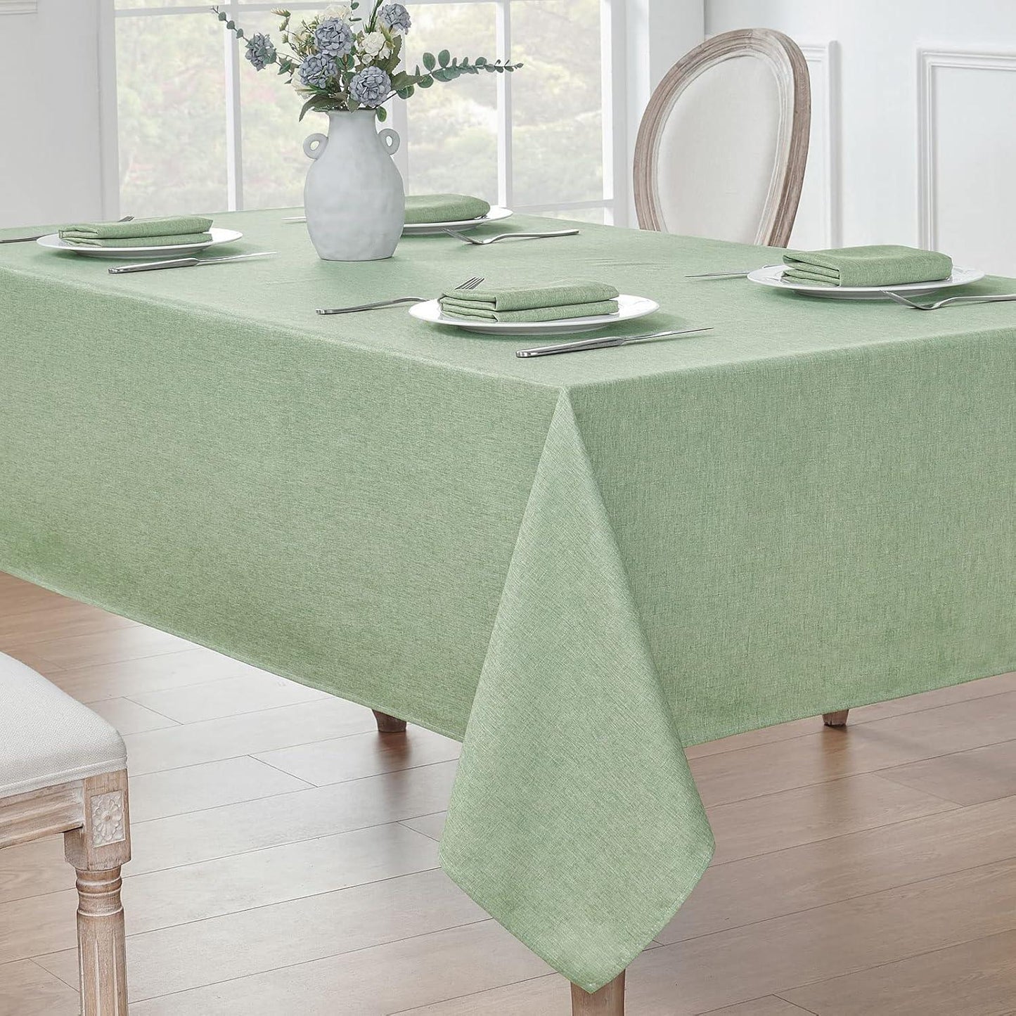 Rectangular dining table with sage green waterproof linen textured tablecloth set with plates, napkins, and silverware