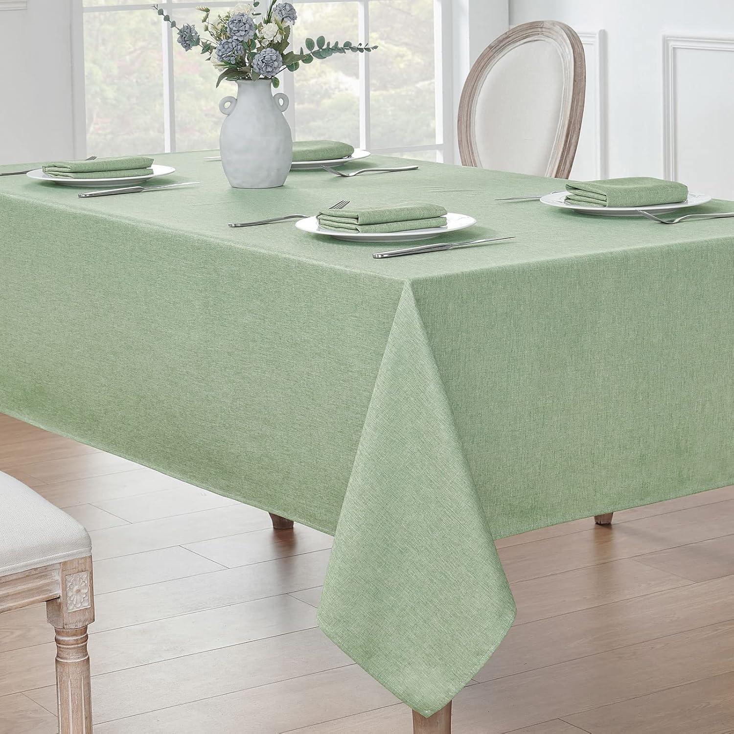 Rectangular dining table with sage green waterproof linen textured tablecloth set with plates, napkins, and silverware