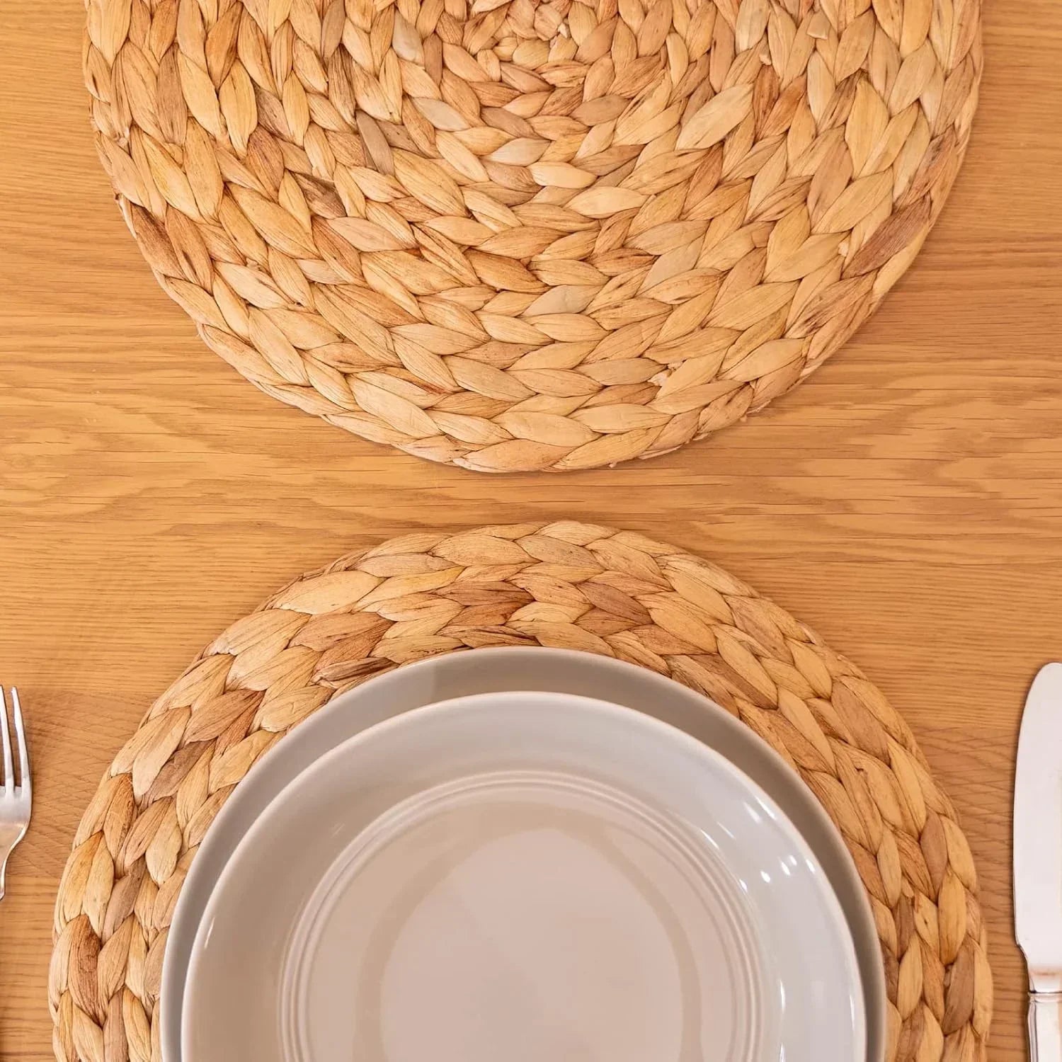 Set of 4 round natural woven water hyacinth placemats on wooden table with beige plates