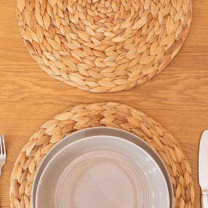 Set of 4 round natural woven water hyacinth placemats on wooden table with beige plates
