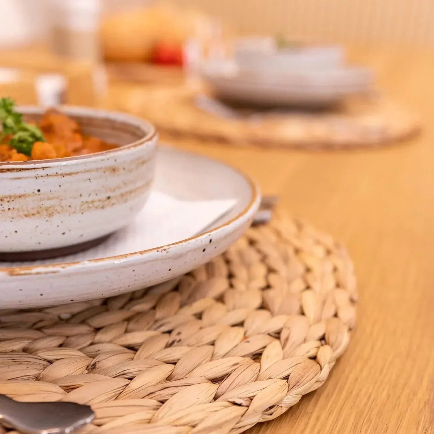 Set of 4 natural water hyacinth round woven placemats on a wooden table with ceramic bowls and plates