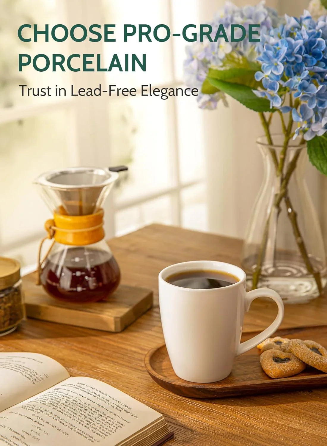 White porcelain coffee mug on wooden tray with cookies, coffee brewer, open book, and blue flowers