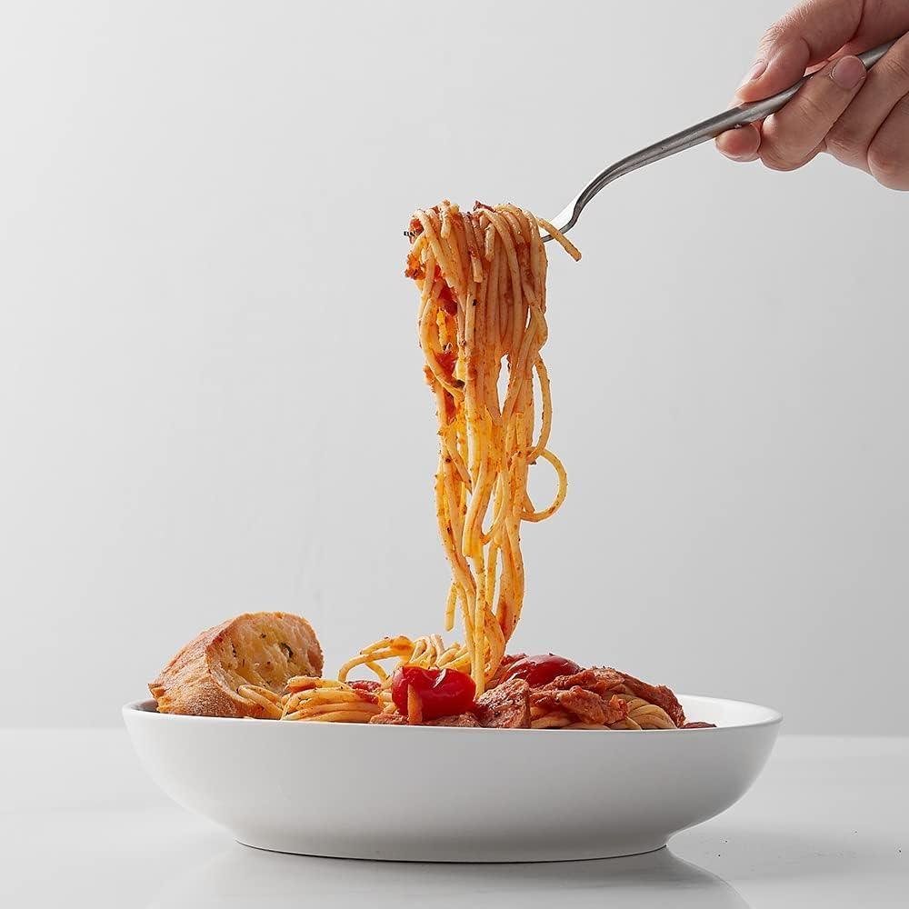 Hand lifting spaghetti with tomato sauce from white shallow pasta bowl with bread slice on white surface