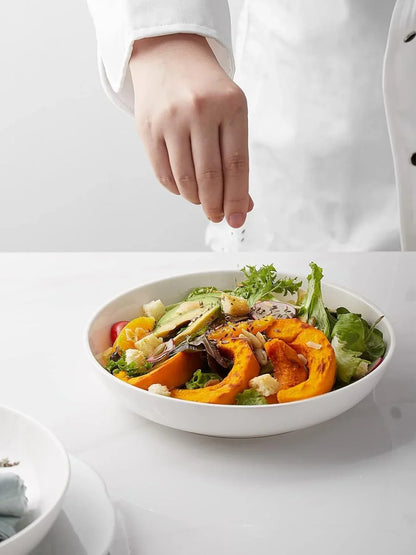White porcelain pasta bowl with fresh mixed salad including greens, roasted pumpkin, avocado, and croutons