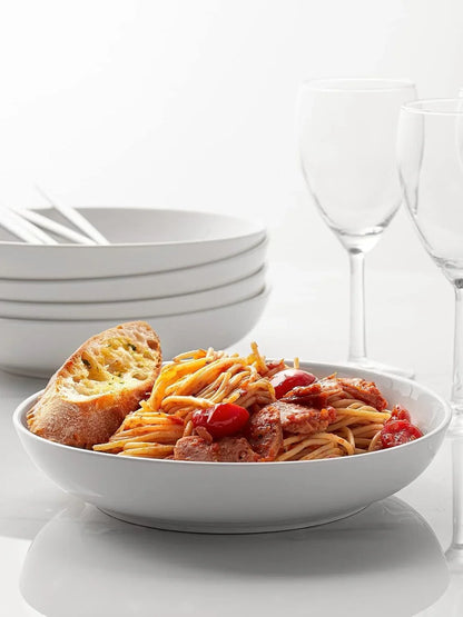 White porcelain wide shallow pasta bowl with spaghetti, cherry tomatoes, sausage, and garlic bread on white surface
