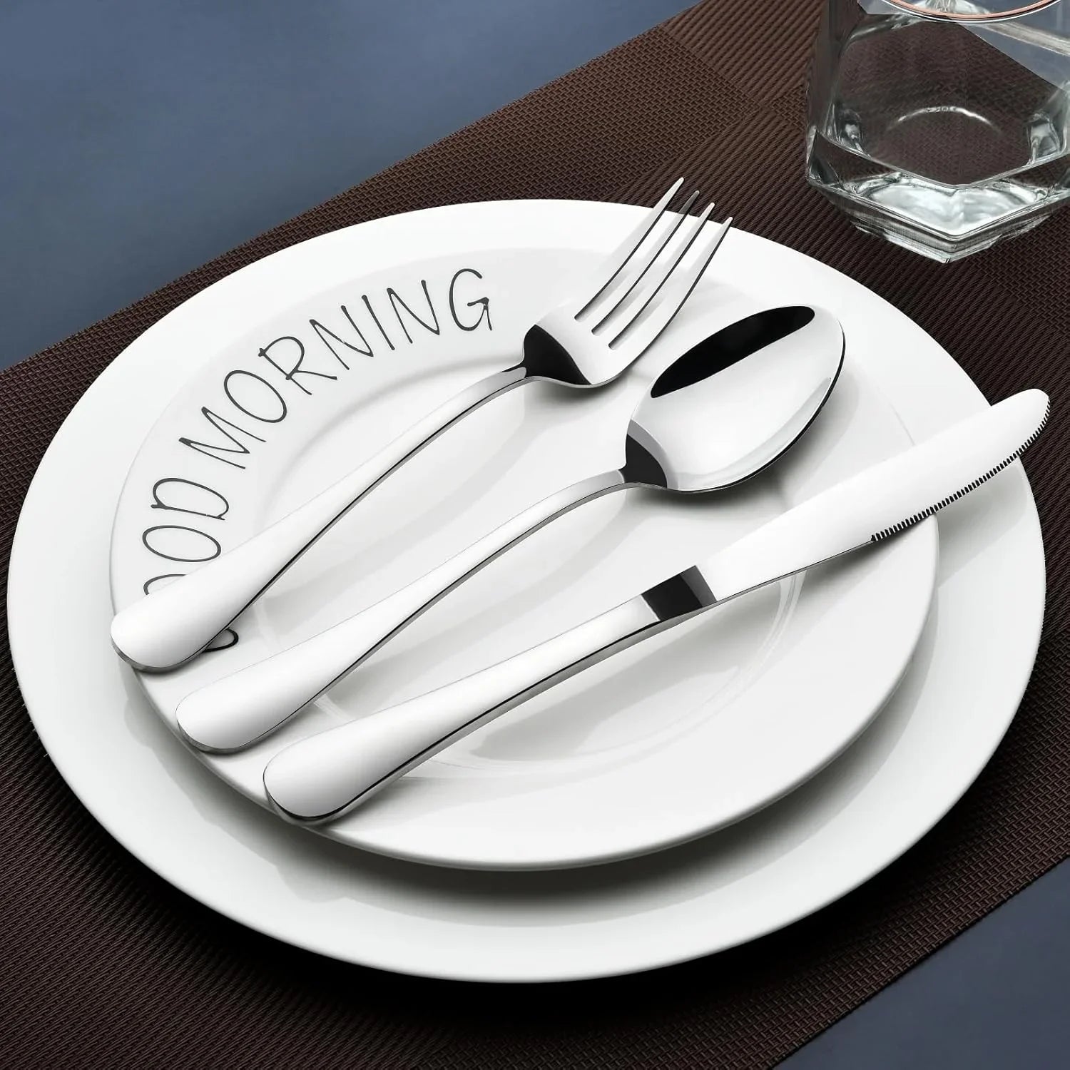 Silver stainless steel fork, spoon, knife on white plates with 'Good Morning' text on a dark placemat