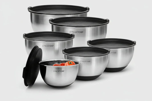 Set of six stainless steel mixing bowls with black lids and non-slip bases, one bowl contains tomatoes