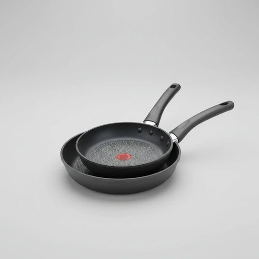 Two black hard anodized nonstick frying pans with heat indicator on gray background